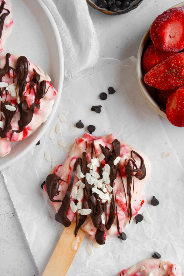 A top down shot pf a strawberry popsicle drizzled with chocolate and sprinkled with coconut.