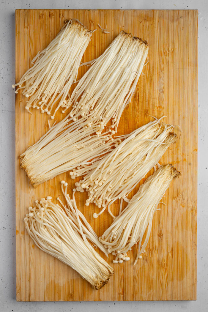 Enoki mushroom clusters on a cutting board.