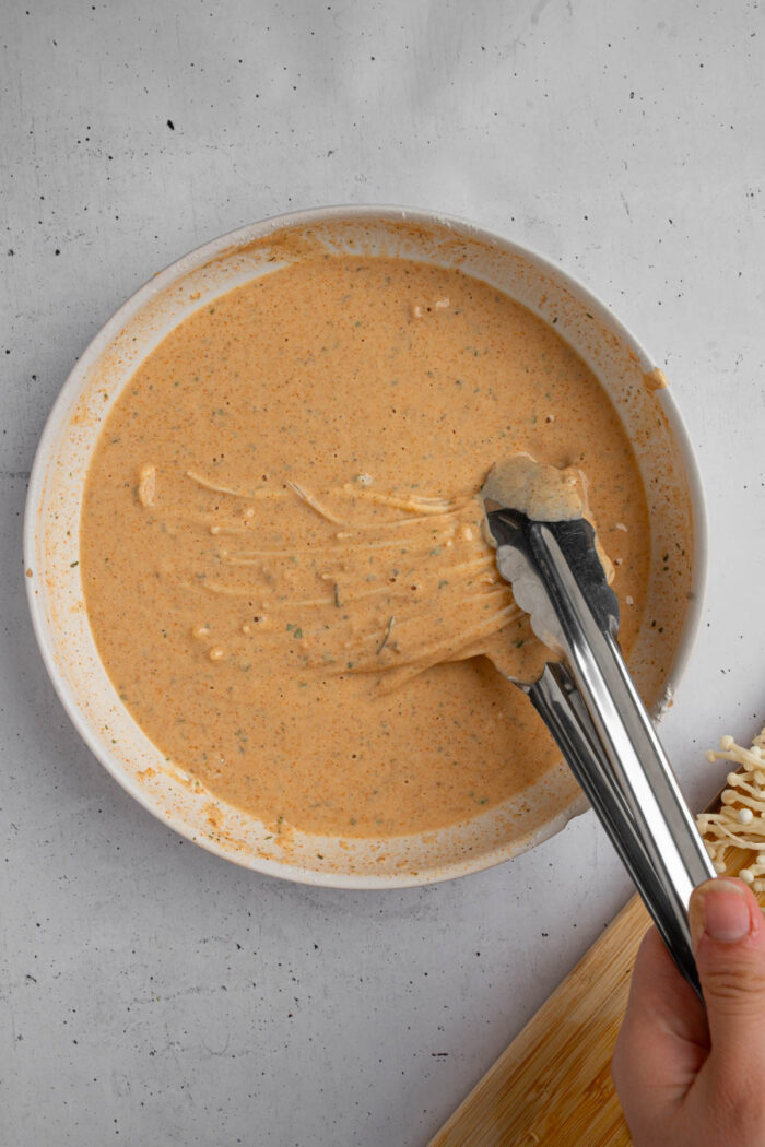 Enoki being fully coated in the spiced batter to make vegan fried chicken.