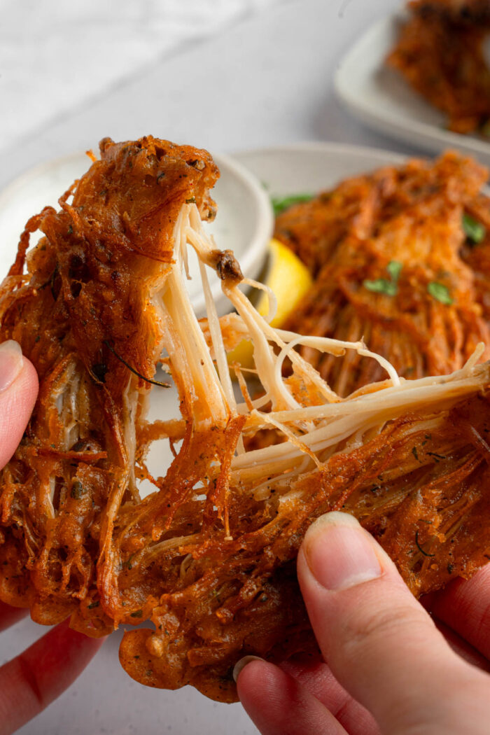 A close up shot of vegan fried chicken being torn into strands, exposing the enoki base.