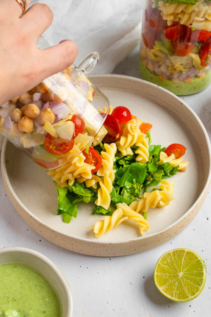 Pesto pasta salad being poured from the jar onto a plate.