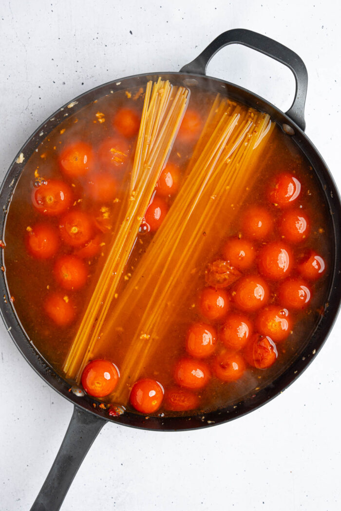 Spaghetti and water added to the same cast iron pan as tomatoes and garlic.