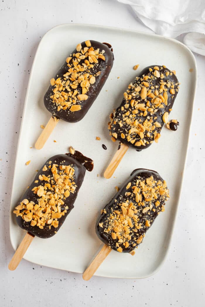 Four healthy homemade ice cream bars rested on a plate for the chocolate to set.