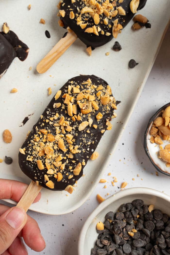 A tray with healthy homemade ice cream bars coated in chocolate and covered with crushed peanuts.