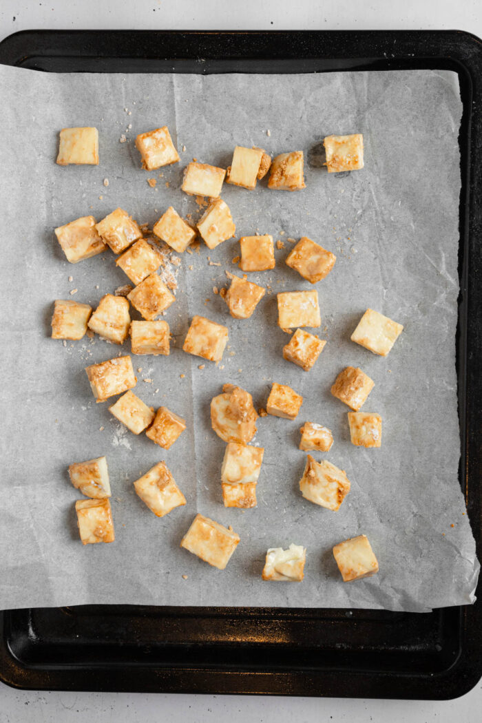Tofu cubes in marinate spread on a lined baking sheet.