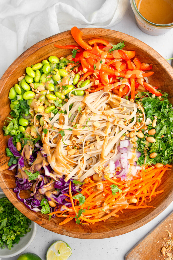 A large salad bowl of Thai noodle salad with peanut dressing drizzled over the top.
