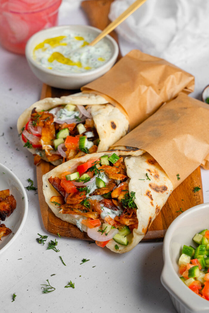 Two wraps of vegan shawarma in parchment paper served with plant based tzatziki.