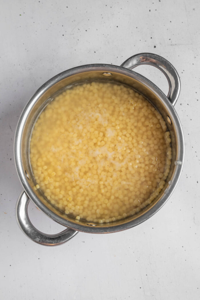 Pearl couscous in a steel pot, cooking according to the package instructions.