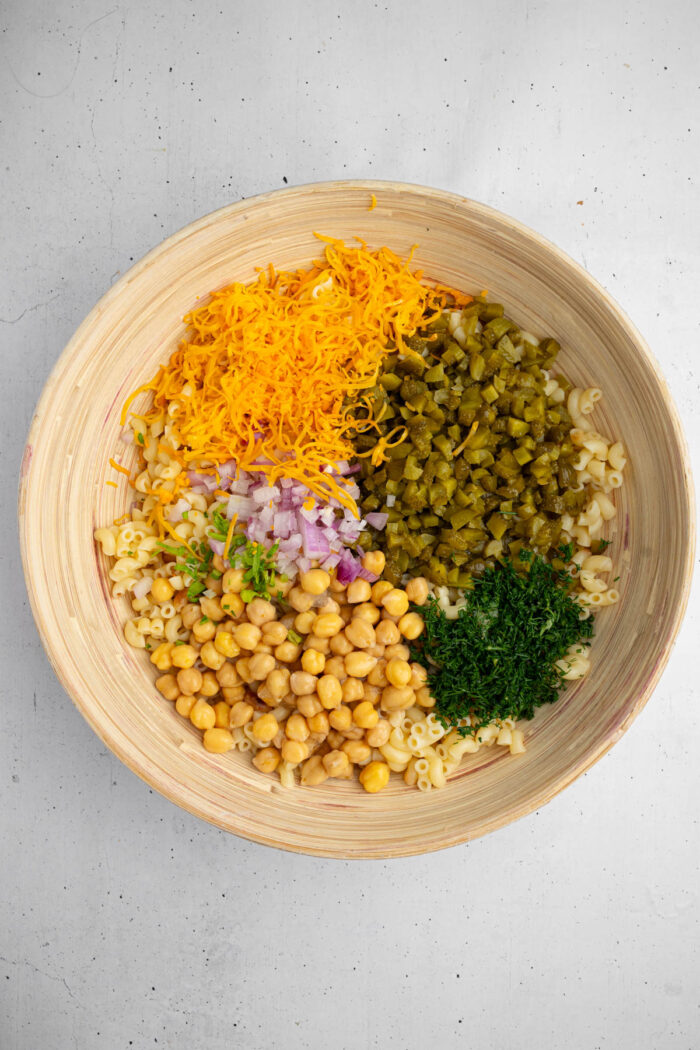 Chopped and cooked ingredients of the dill pickle pasta salad in a large mixing bowl.