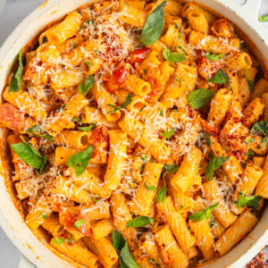 A large ceramic skillet filled with creamy tomato pasta, served with fresh basil and vegan cheese shot from above.