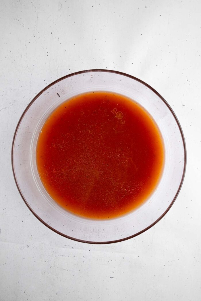 Tomato sauce ingredients whisked together in a glass bowl.