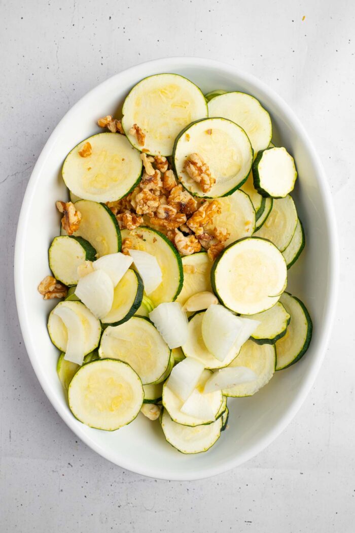 Sliced zucchinis and aromatics in a casserole dish.