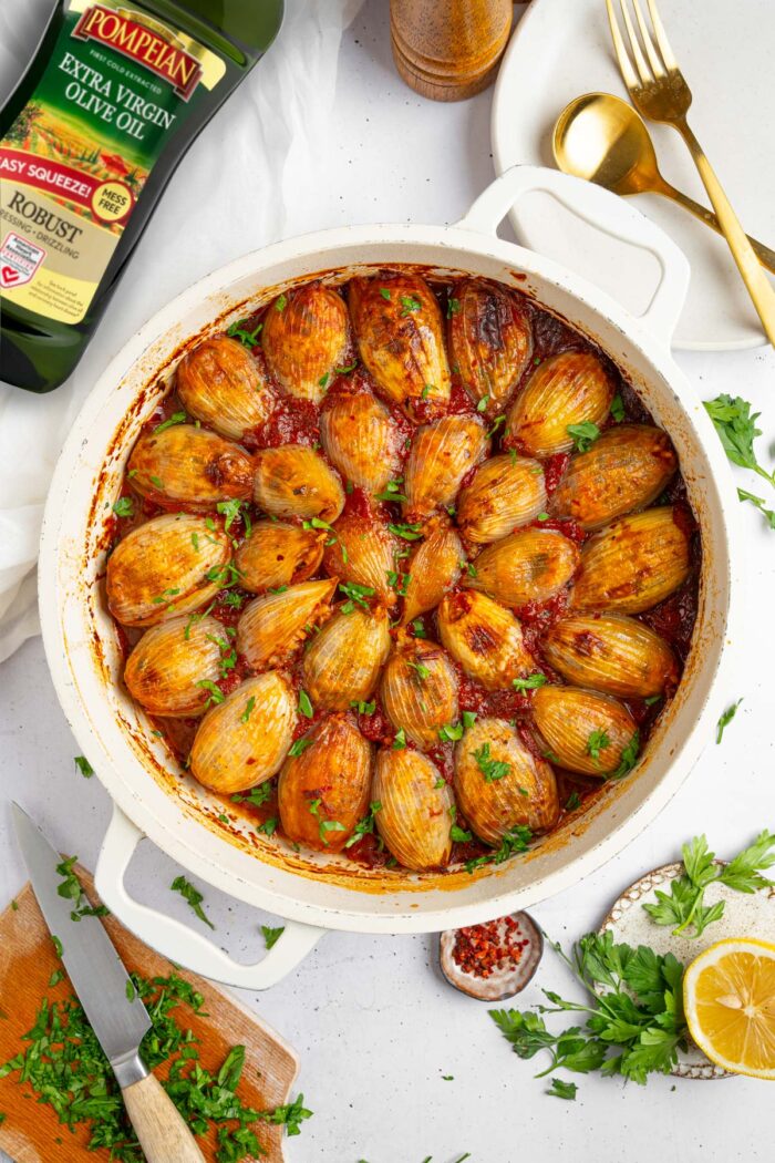 Stuffed onions in the baking pan, served with fresh herbs.