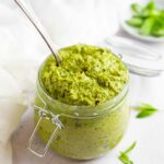 A swingtop mason jar filled with vegan zucchini pesto and a spoon sticking out.