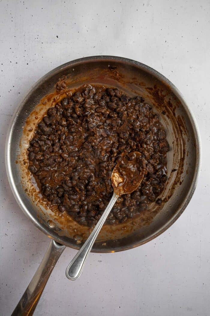 A frying pan with garlic, black beans, and taco seasoning cooked together as a filling for sheet pan crunchwraps.