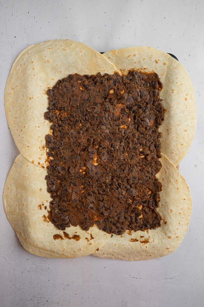 Tortillas laid out in a consistent layer, with the black bean mixture spread in the middle.