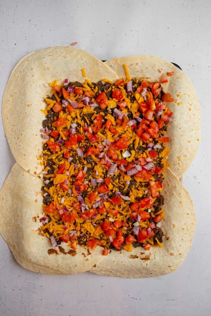 Fresh tomatoes and onions added on top of tortilla cheese for sheet pan crunchwraps.