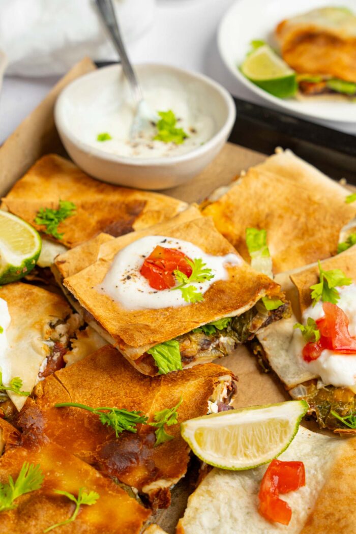 A serving of sheet pan crunchwrap stacked on top of other squares, with added vegan sour cream.