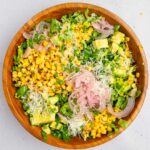 All of the ingredients added to a large wooden salad bowl and topped with vegan cheese.