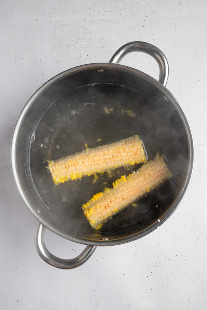 Corn cobs in boiling water in a steel pot.