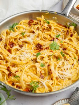 A pan featuring the entire dish of creamy corn pasta, with some vegan parmesan and fresh herbs on top.