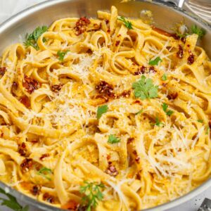 A pan featuring the entire dish of creamy corn pasta, with some vegan parmesan and fresh herbs on top.