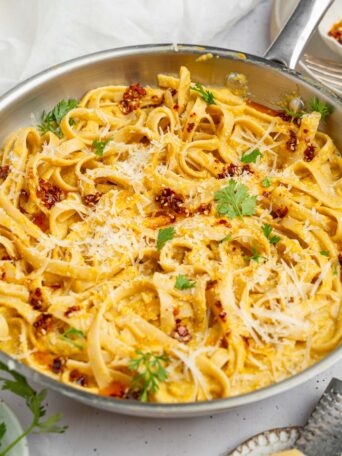 A pan featuring the entire dish of creamy corn pasta, with some vegan parmesan and fresh herbs on top.