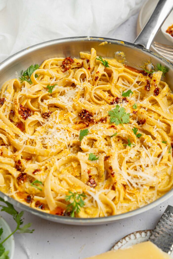 A pan featuring the entire dish of creamy corn pasta, with some vegan parmesan and fresh herbs on top.