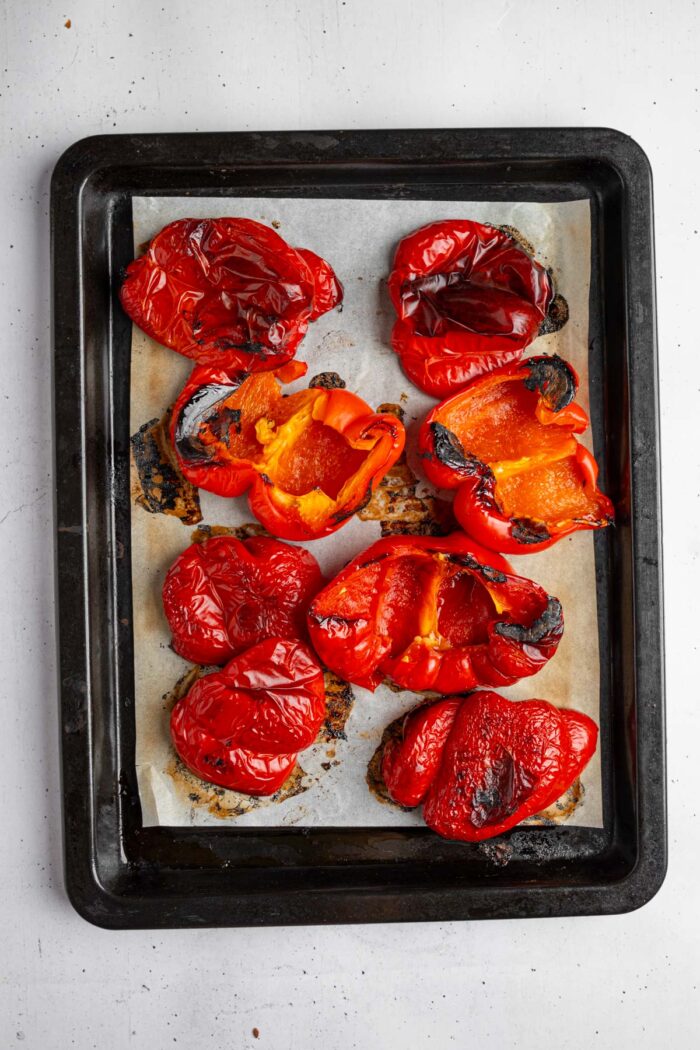 Roasted, slightly charred red bell peppers on a lined baking sheet.