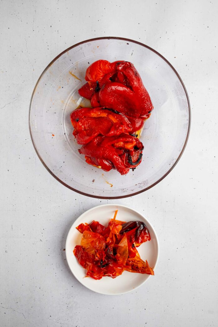 A bowl with roasted red peppers, and a discard bowl with the peeled off skins.