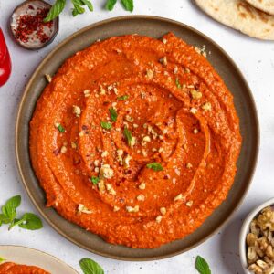 Roasted red pepper walnut dip served beautifully on a platter, sprinkled with some crushed walnuts and fresh herbs.