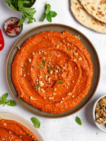 Roasted red pepper walnut dip served beautifully on a platter, sprinkled with some crushed walnuts and fresh herbs.