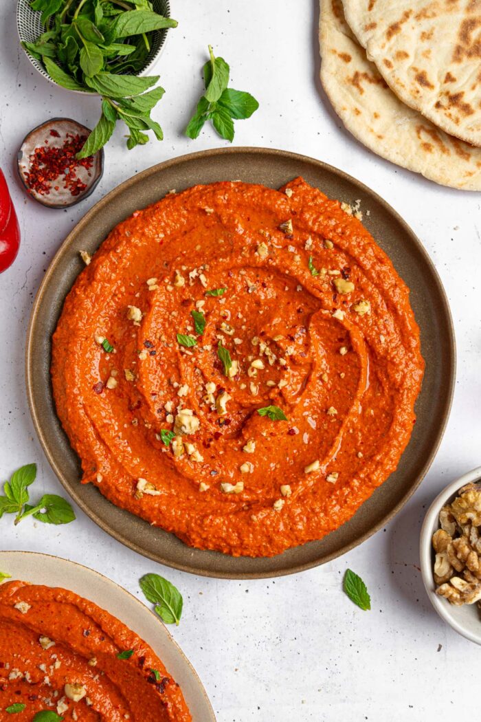 Roasted red pepper walnut dip served beautifully on a platter, sprinkled with some crushed walnuts and fresh herbs.