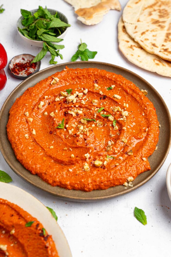 Roasted red pepper walnut dip served beautifully on a platter, sprinkled with some crushed walnuts and fresh herbs.