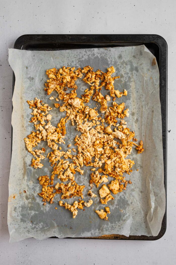 Slightly browned shredded tofu on a lined baking sheet after cooking.