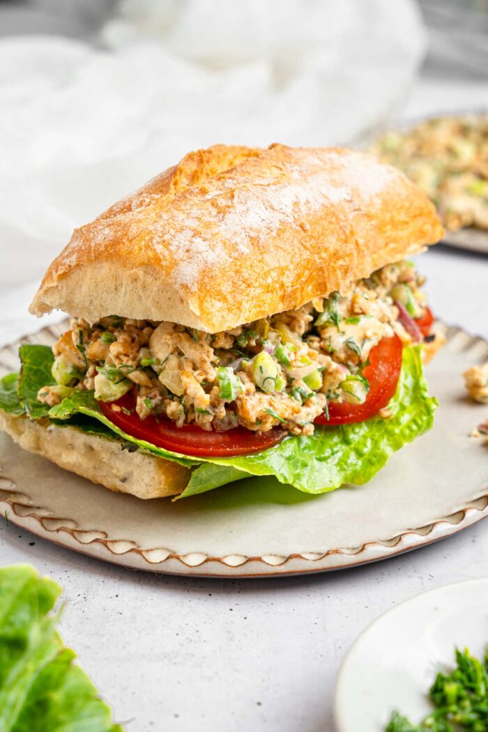 Vegan chicken salad sandwich on a white ceramic plate, made with lettuce, tomato, and ciabatta.