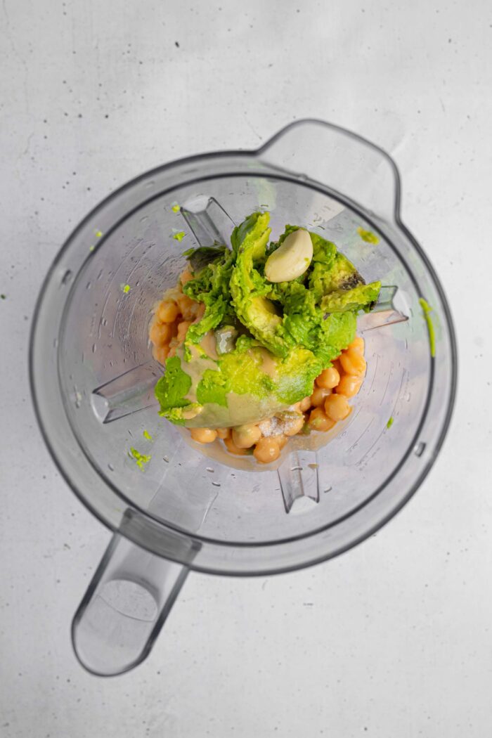 Hummus, chickpeas, tahini, and other ingredients to make avocado hummus added into a high-speed blender.