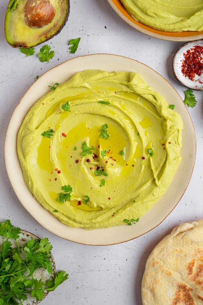 Avocado hummus on a serving plate, topped with olive oil, fresh parsley, and red pepper flakes.