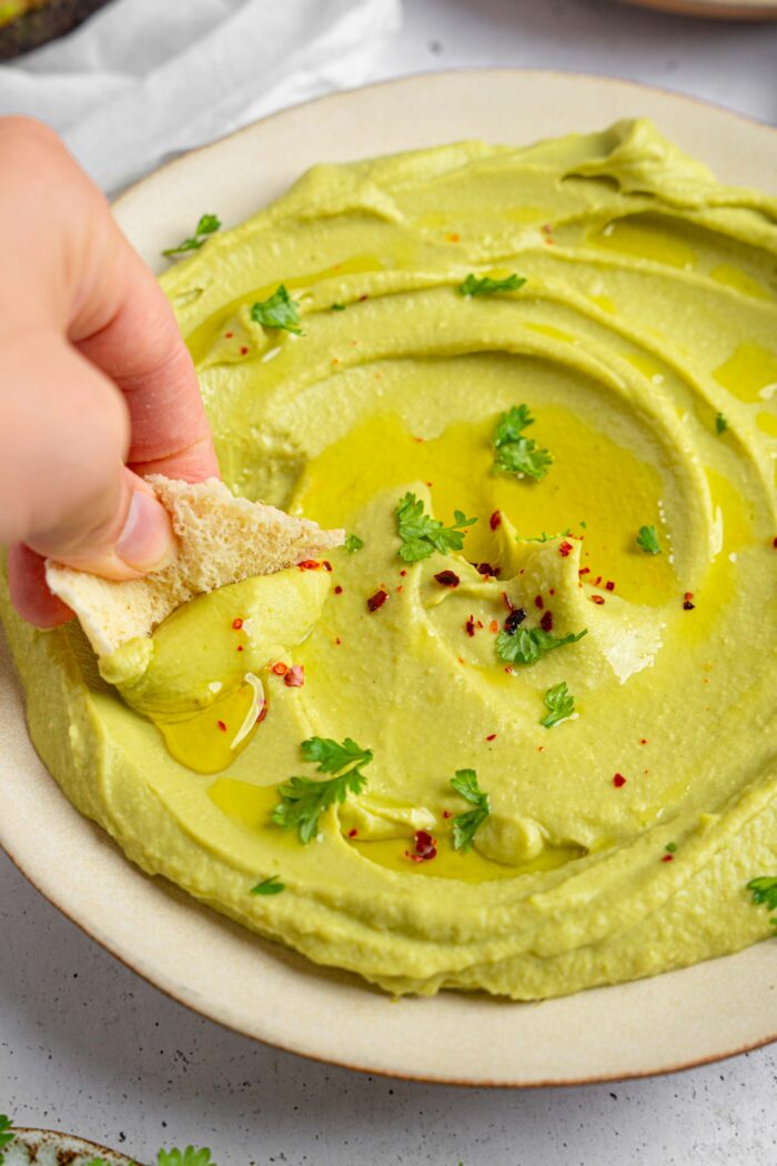 A piece of flatbread being dipped into avocado hummus.