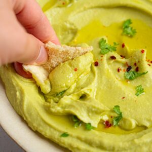 A close image of flatbread being dipped into avocado hummus.