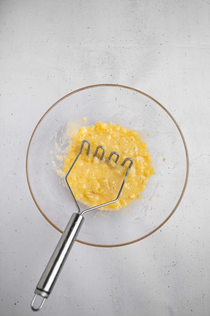 Mashed up ripe bananas in a glass mixing bowl.