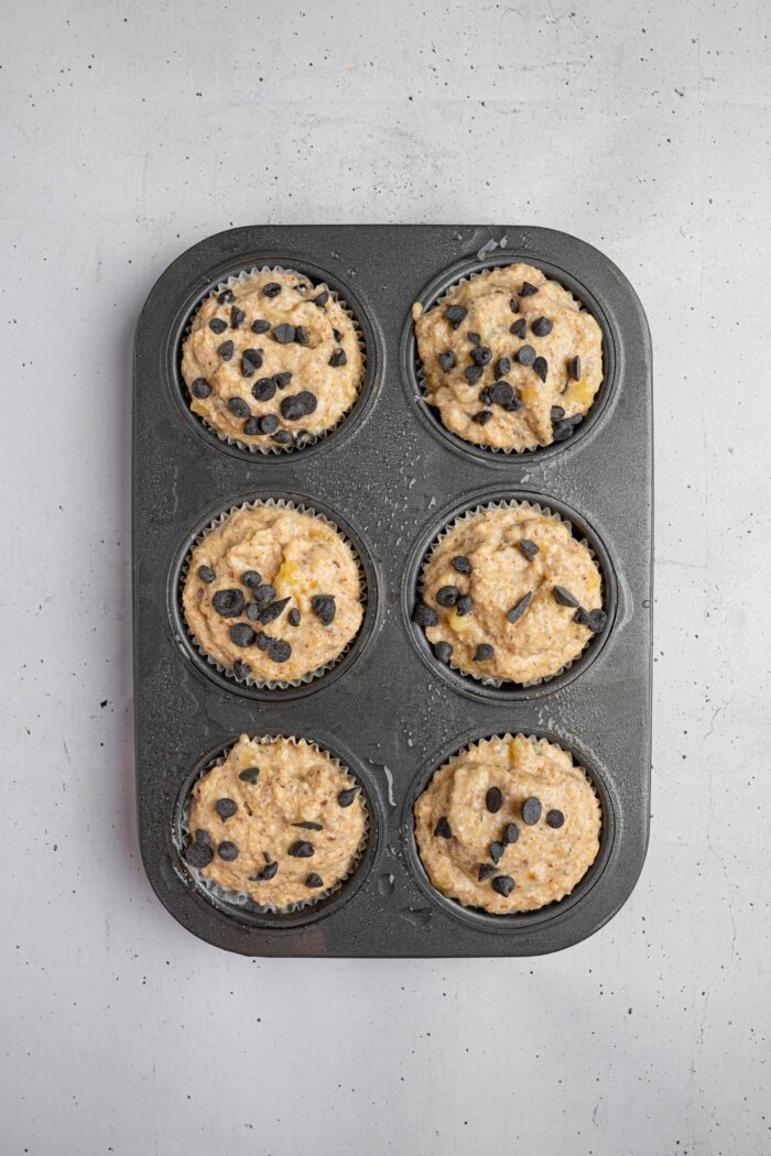 A muffin tray with equal amounts of banana oatmeal muffin batter in each cup.