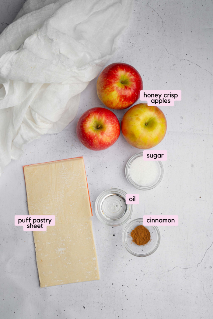 Five ingredients to make puff pastry apple donuts, laid out and labeled on a light background.