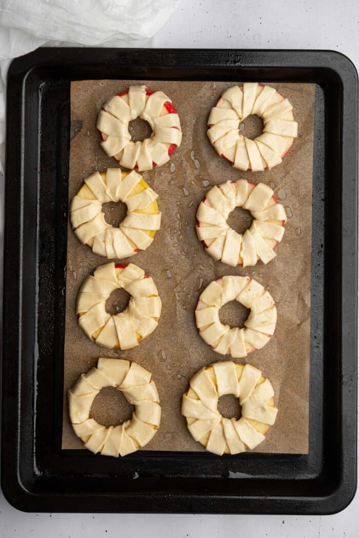 A baking sheet linedwith parchment, with eight apple "donuts" laid out evenly.