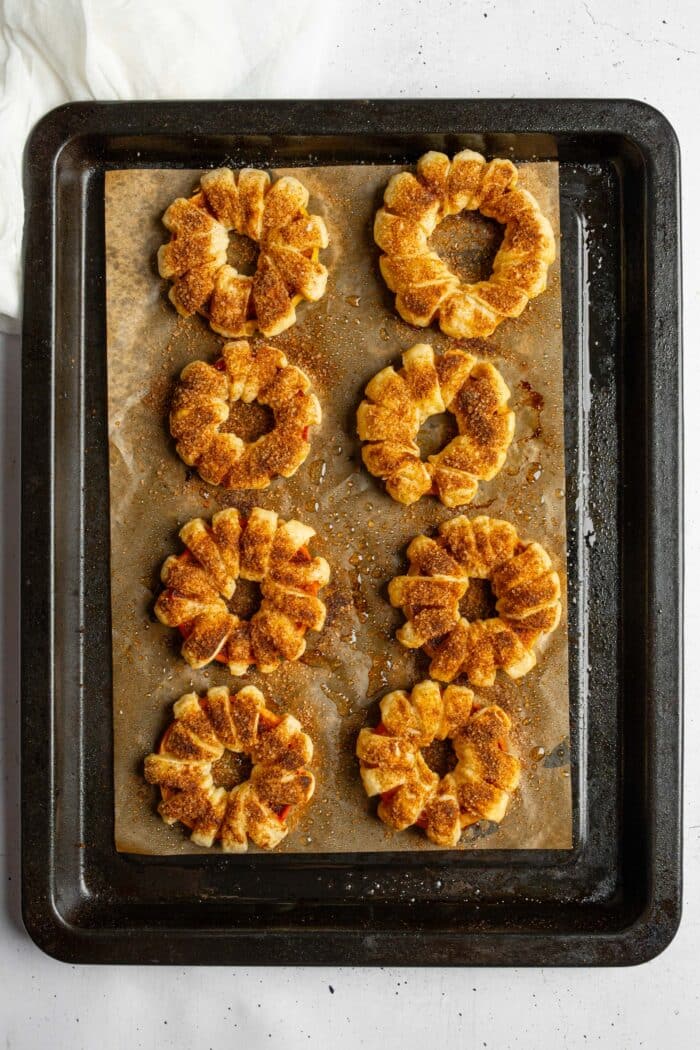 Freshly baked puff pastry apple donuts, still on a lined baking sheet.