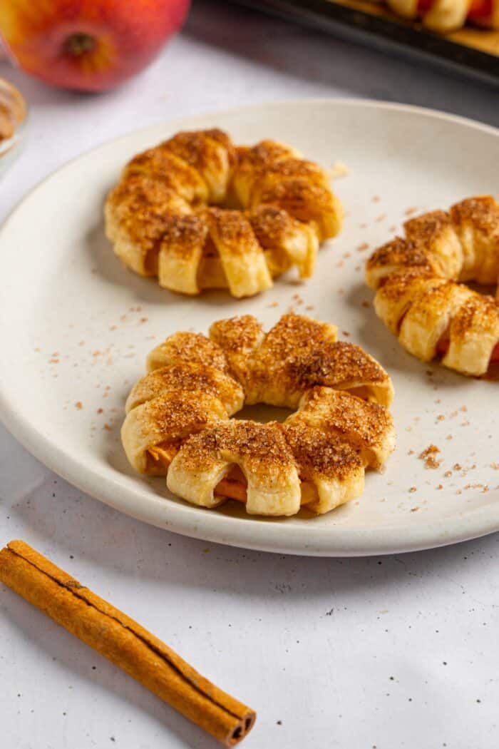 A close shot of puff pastry apple donuts on a white ceramic plate.