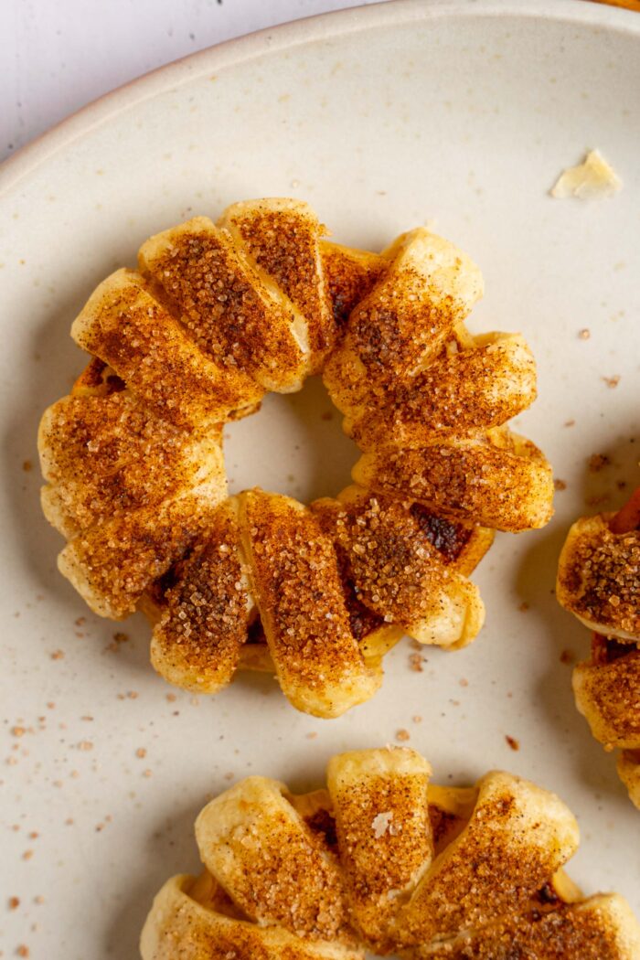 A close view of one puff pastry apple donut coated in cinnamon sugar.
