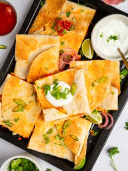 A batch of buffalo cauliflower quesadillas served on a black platter for game day.