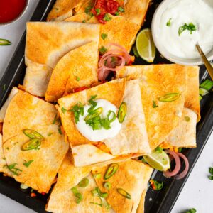 A batch of buffalo cauliflower quesadillas served on a black platter for game day.