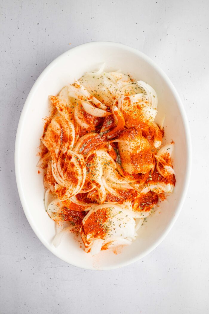 Thinly sliced onions in a casserole pan with spices and other seasonings.